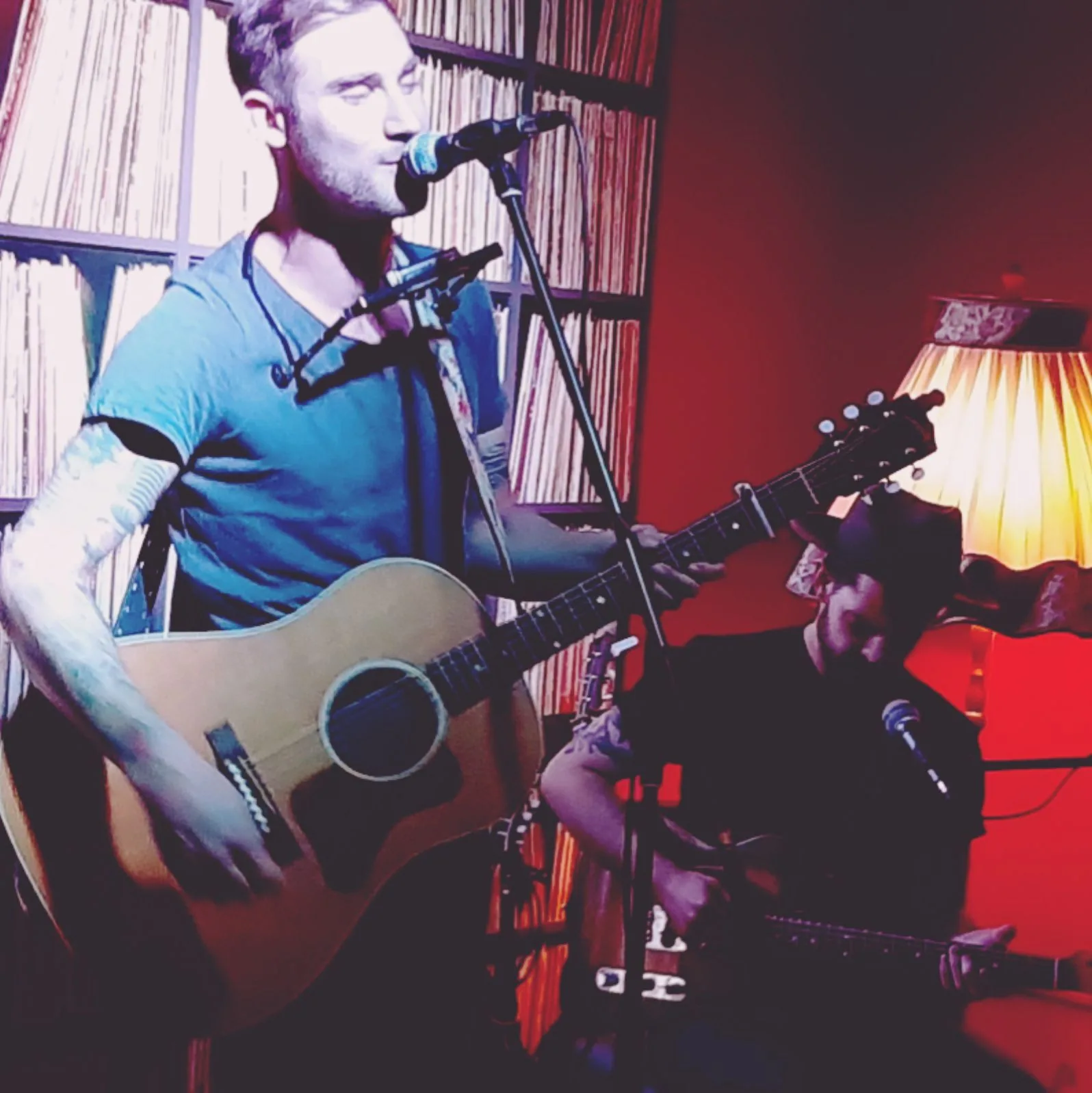 Brickwater live in rotem Licht vor einer Plattenwand, mit Gitarre und Mundharmonika